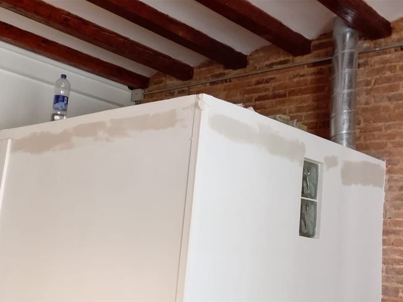 Tabique de obra nueva rematado en blanco bajo un techo de vigas de madera y pared de ladrillo visto